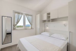 Ein Schlafzimmer mit Bett, einem Fenster mit Vorhängen, einem Spiegel und eingebauten Regalen.