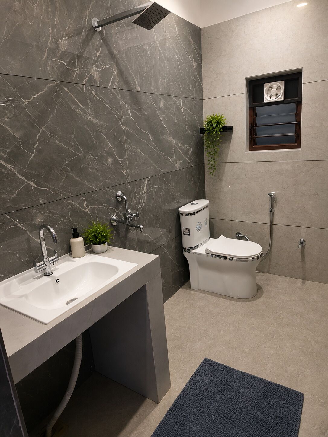 A modern bathroom with a marble wall, a white sink, a toilet, a shower, and a small shelf with a plant.