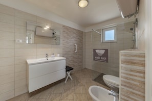 A modern bathroom with a white vanity, a bathtub, a toilet, and a shower area. - Wabi Sabi Apartment 6 (Krk)