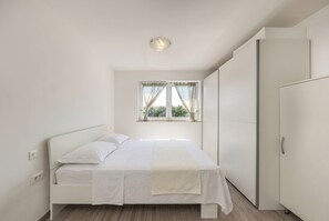 A bedroom with a bed, a window with curtains, a wardrobe, and a ceiling light. - Wabi Sabi Apartment 6 (Krk)