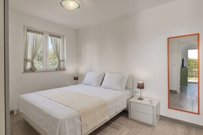 Ein Schlafzimmer mit einem Bett, Nachttischen, einem Spiegel und einem Fenster mit Vorhängen.
