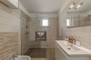 Ein modernes Badezimmer mit Dusche, Waschbecken und Toilette. Über der Dusche befindet sich ein kleines Fenster, und die Wände sind mit Fliesen versehen.