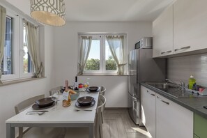 Eine moderne Küche mit Essbereich, Edelstahlgeräten und Blick auf Grünfläche.