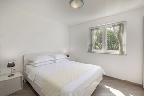 Ein Schlafzimmer mit Bett, Nachttisch, Lampe und einem Fenster mit Vorhängen.