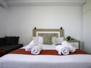 Ein Hotelzimmer mit Bett, Nachttisch, einer kleinen Pflanze und einem dunkelgrauen Sofa.