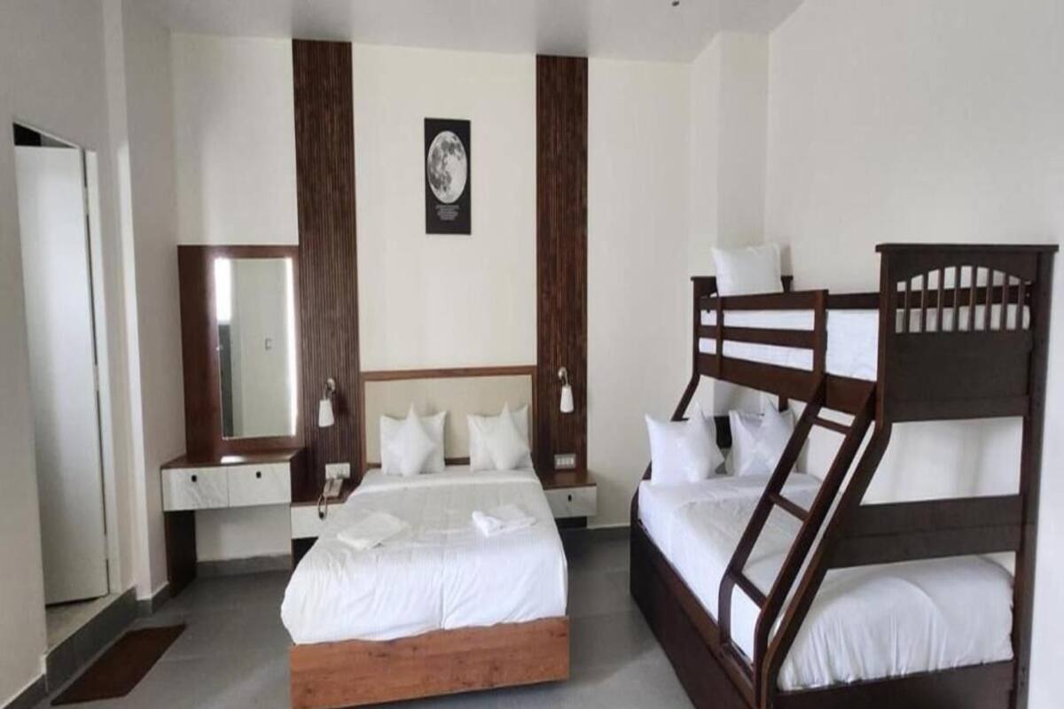 A hotel room with a large bed, a smaller bed, a bunk bed, a mirror, and a wall-mounted picture.