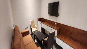 A small, modern room with a sofa, a table, a chair, a TV mounted on the wall, and a wooden bench.
