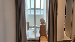 A room with a sliding glass door leading to a balcony with a chair and a small table.