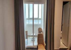 Una habitación con puerta de vidrio corrediza que da a un balcón con una silla y una mesita.