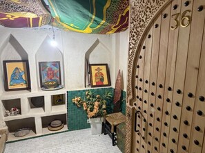 Una habitación con pared de azulejos verdes, una puerta de madera con un número y cuadros enmarcados en la pared.