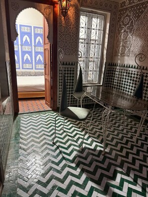 A room with a herringbone floor pattern, a bench with cushions, a decorative wall, and a window with metal bars. - Renovated riad near Jemaa el FnaQuiet stay (Marrakesh)