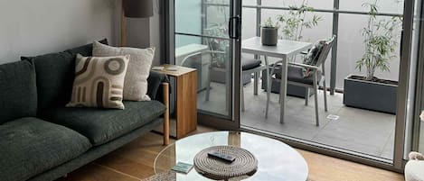 A modern living room with a sofa, a glass coffee table, and a view of an outdoor balcony with plants.
