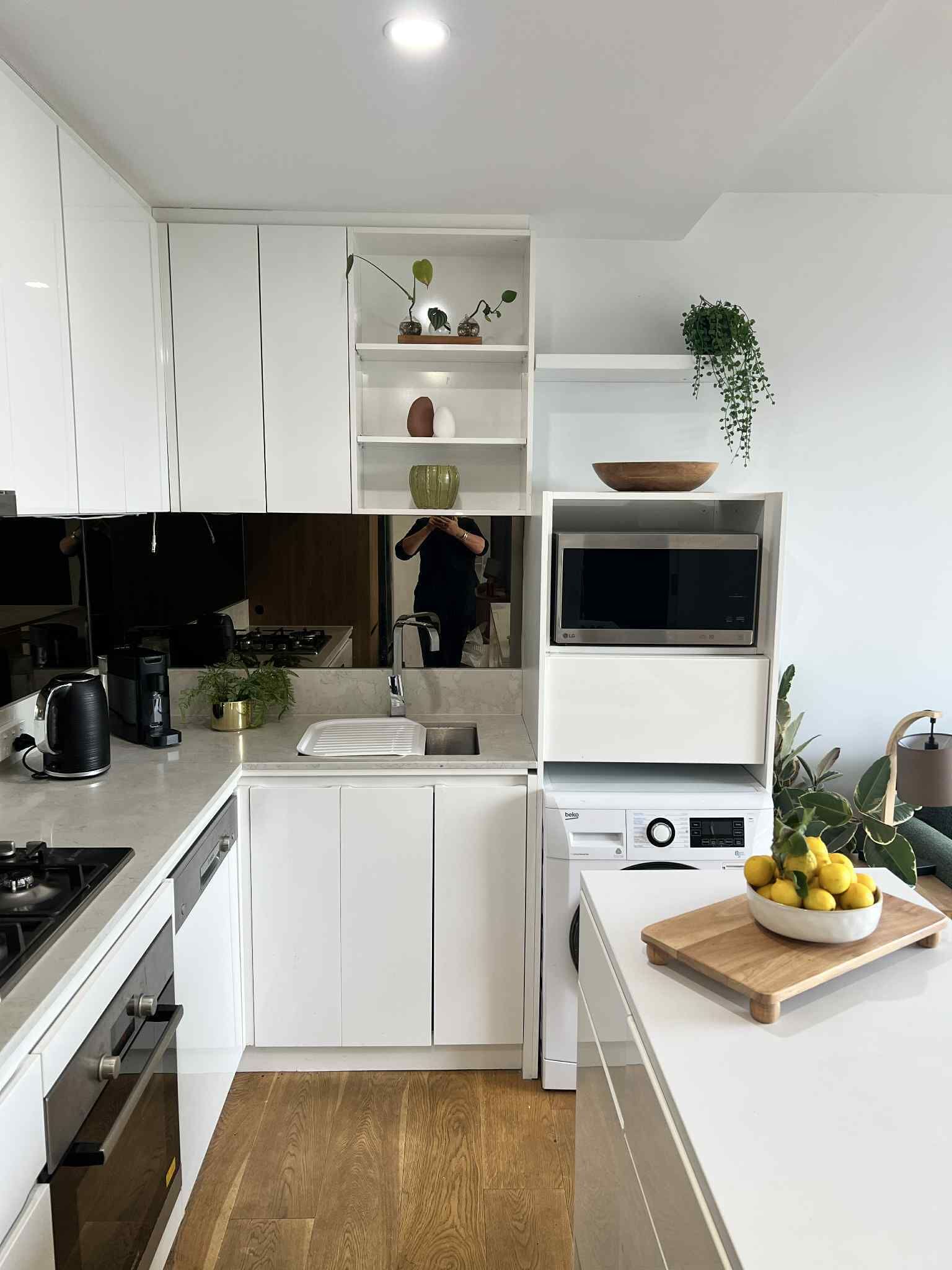 A modern kitchen with white cabinets, a built-in oven, a microwave, and a sink.