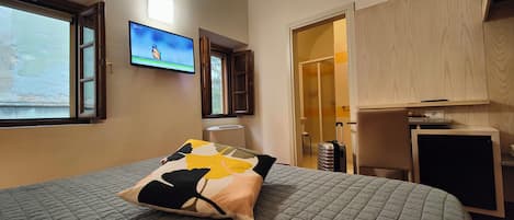 A hotel room with a bed, a television on the wall, a suitcase, and a wooden cabinet.