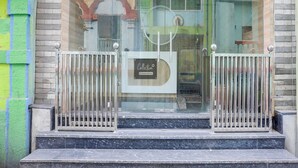 Entrada de un edificio con puerta de vidrio, rejas de metal y un cartel que dice 'Collection'.