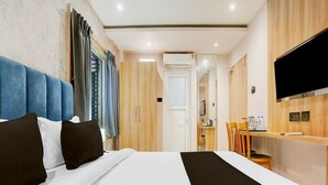 Habitación de hotel con cama, escritorio, silla, televisión y puerta de baño.