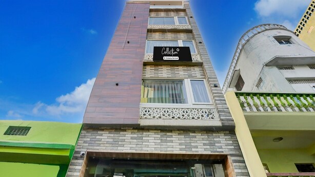 Un edificio de varios pisos con un llamativo letrero 'Collection', una gran entrada de vidrio y un balcón con barandilla verde.