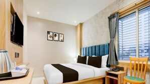 Habitación de hotel con cama, escritorio con hervidor, una silla y ventana con persianas.