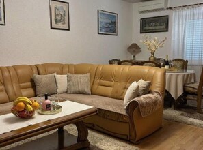Ein Wohnzimmer mit einem braunen Ledersofa, einem Couchtisch mit Früchten und einem Essbereich mit Tisch und Stühlen.