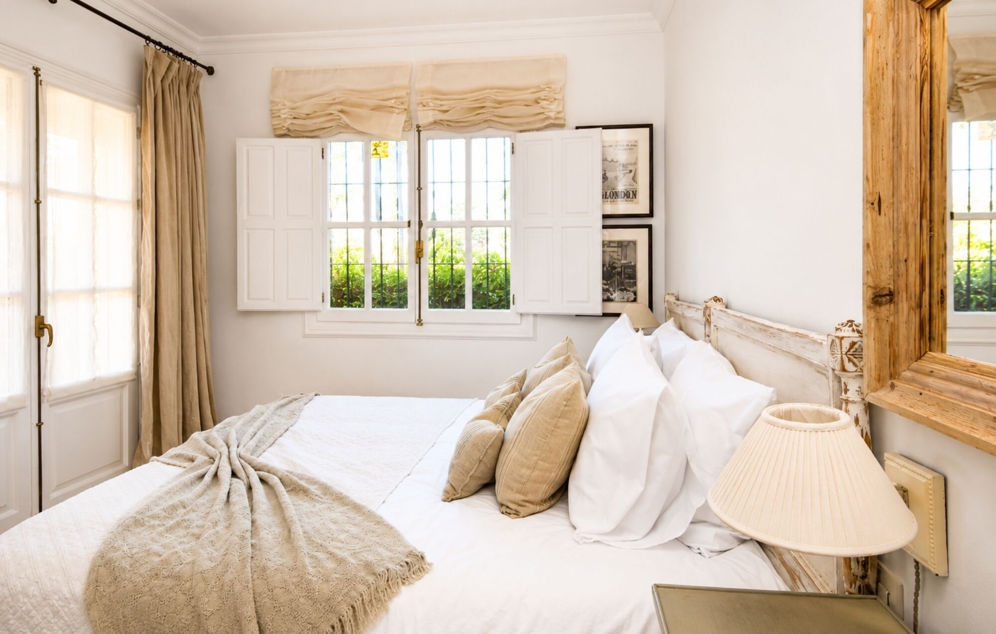 Un dormitorio con cama, ventana con cortinas, lámpara y espejo.