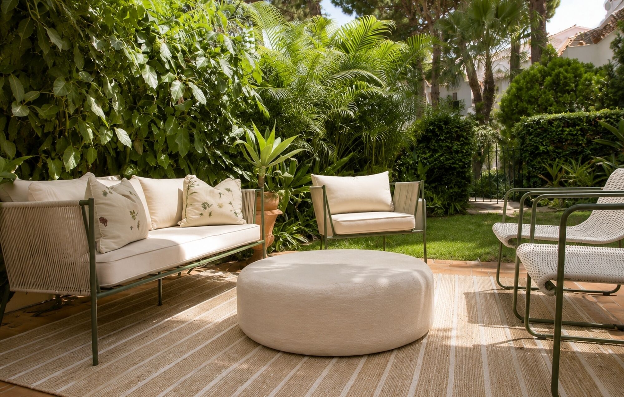 Une terrasse agrémentée d’un canapé, d’un pouf et de fauteuils, le tout entouré d’une végétation luxuriante.