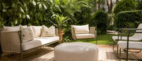 Un patio con sofá, reposapiés y sillas, rodeado de exuberante follaje.