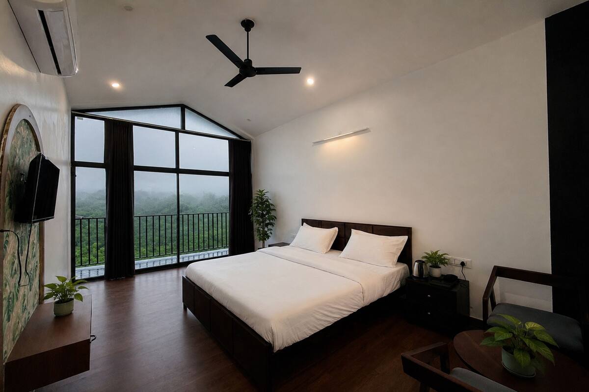 A bedroom with a bed, a ceiling fan, a TV, a nightstand, a chair, and a large window with a view.