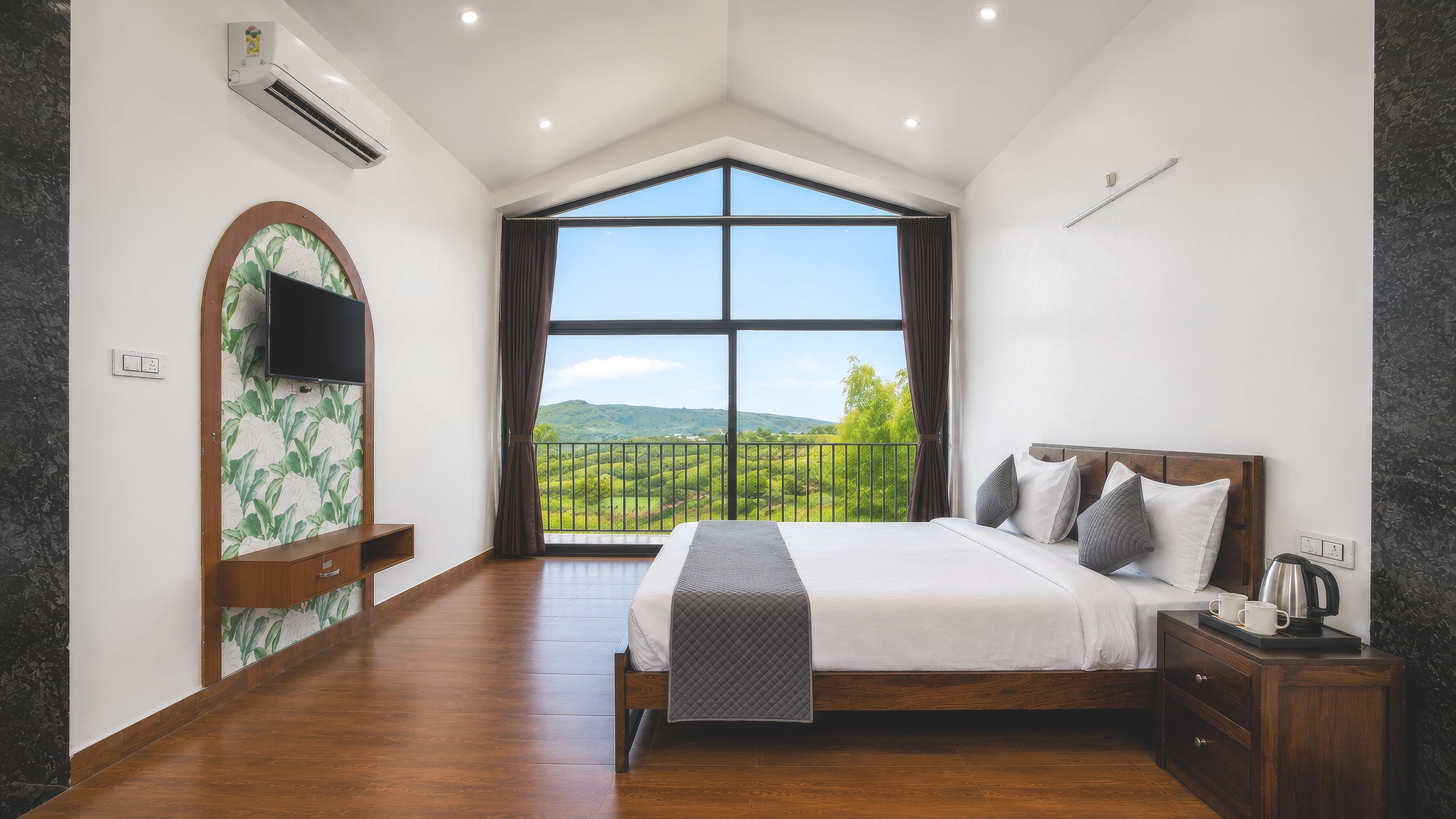 A bedroom with a large window, a bed, a TV, and a wooden nightstand.