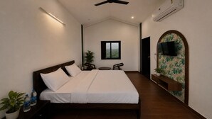 Une chambre comprenant un lit, des tables de chevet, un ventilateur de plafond, un appareil de climatisation, un téléviseur et un petit coin salon agrémenté d’une plante.
