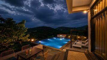 Piscina com vista para as montanhas, área de refeições com cadeiras e área de estar com espreguiçadeiras.