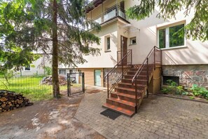 A multi-story building with a staircase leading to a balcony, a stone wall, and a small garden area. - Spacious Apartment for 8 People | Workspace (Sopot)