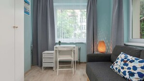 Huoneessa on valkoinen työpöytä, harmaa sohva ja ikkuna, jossa on harmaat verhot.