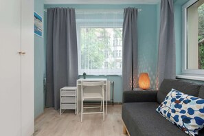 A room with a white desk, a grey sofa, and a window with grey curtains. - Spacious Apartment for 8 People | Workspace (Sopot)
