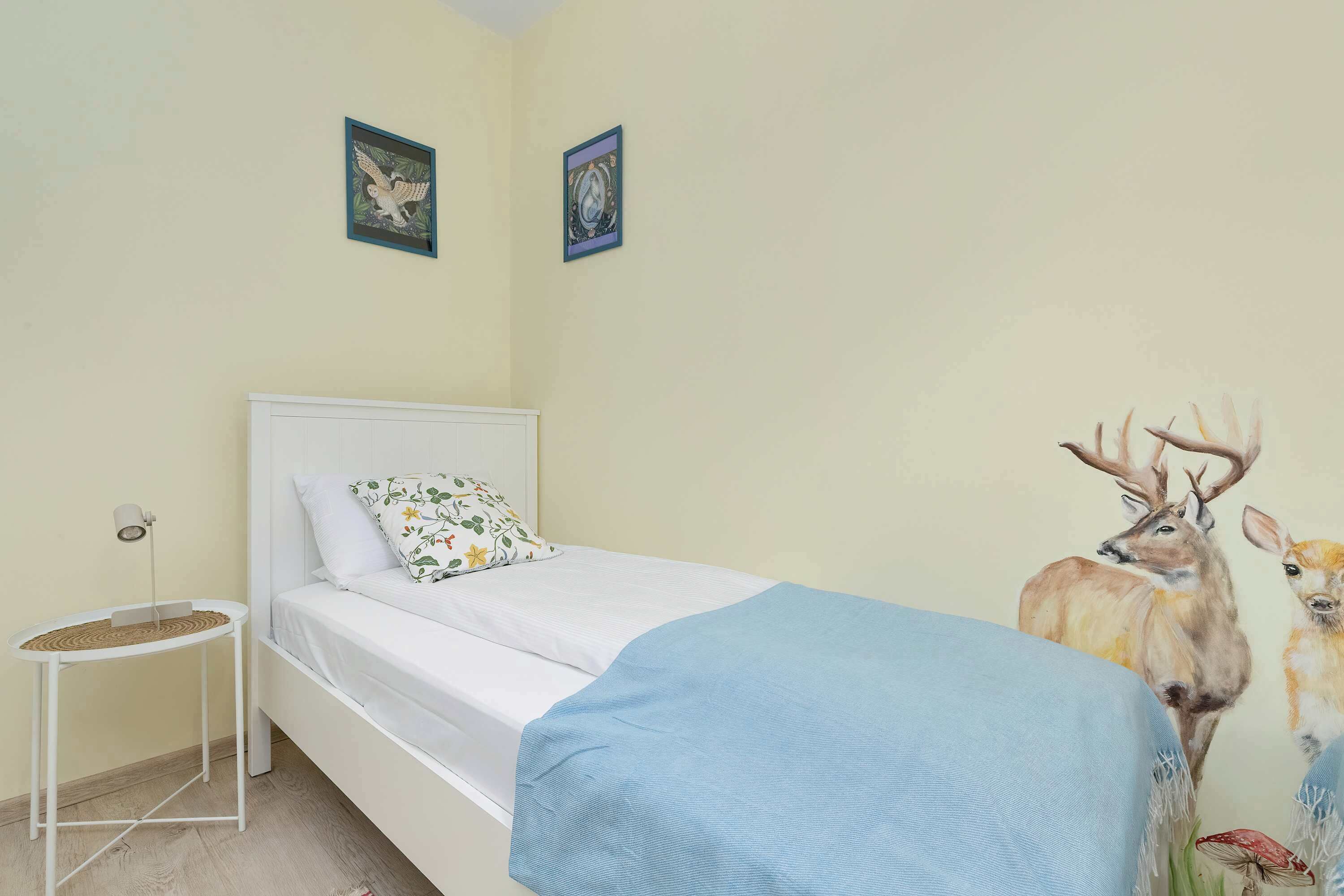 Een slaapkamer met een bed, een nachtkastje, een wandklok en een schilderij van een herten.