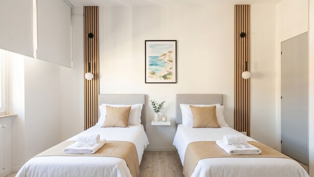 Una habitación de hotel con dos camas, un cuadro en la pared y un pequeño estante con una planta.
