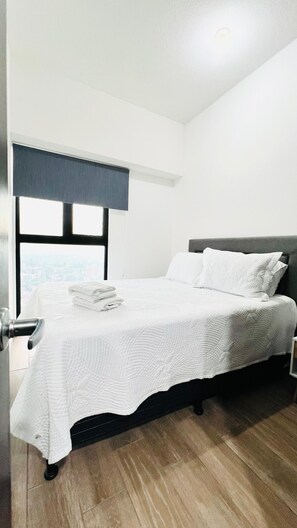 Ein Schlafzimmer mit Bett, Fenster mit Blick, Tür und Deckenlampe.