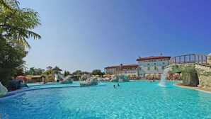 A large outdoor swimming pool with water slides and rock formations, surrounded by umbrellas and a building with a red roof. - Piani Di Clodia 2 p4p Clim (Lazise)