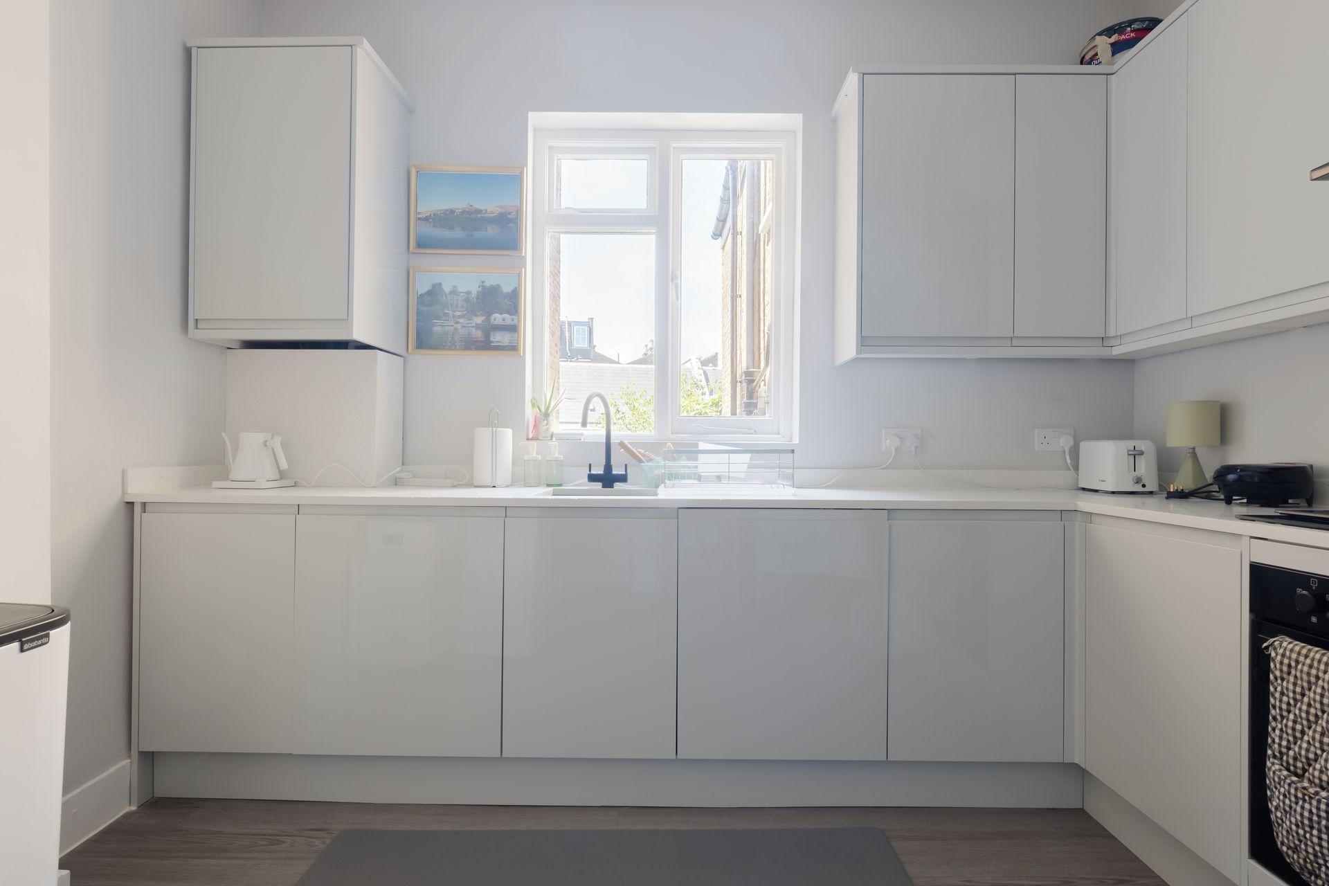 Et moderne køkken med hvide skabe, indbygget ovn og et vindue med naturligt lys.