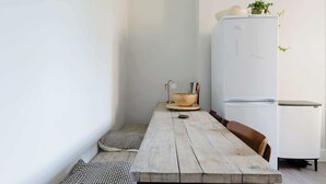 Pieni, käytännöllinen keittiö, jossa on puinen pöytä, valkoinen jääkaappi ja ruukkukasvi.