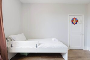 A white bed in a room with a white door and a dartboard on the wall. - Sunny 3BDR Family Home in Clapham (Greater London)