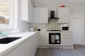 A modern kitchen with white cabinets, a black stove, a microwave, and a dishwasher. - Sunny 3BDR Family Home in Clapham (Greater London)