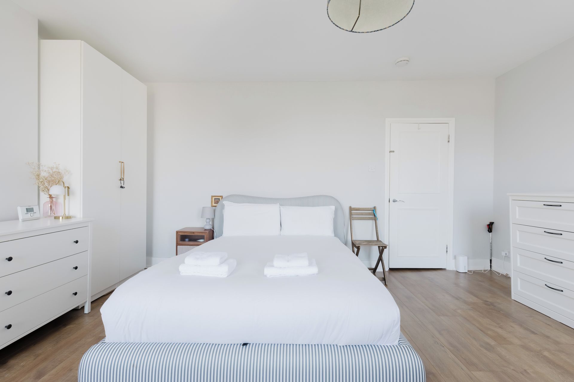 A hotel room with a large bed, a bedside table with a lamp, a chair, and a wardrobe.