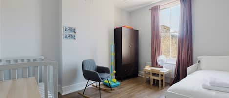 A room with a crib, rocking chair, wardrobe, and a bed.