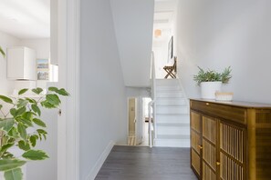 A hallway with a staircase, a wooden cabinet, and a potted plant. - Sunny 3BDR Family Home in Clapham (Greater London)