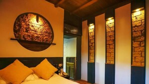 Un dormitorio con cama, almohadas, una lámpara circular fijada a la pared y detalles de pared de piedra.