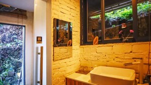 Un baño con un lavamanos blanco, un espejo y una ventana con vistas al verdor.
