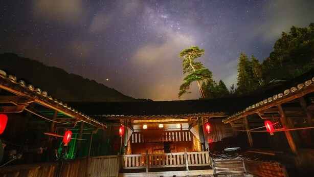 Estructura de madera con balcón y farolillos rojos, bajo un cielo estrellado.