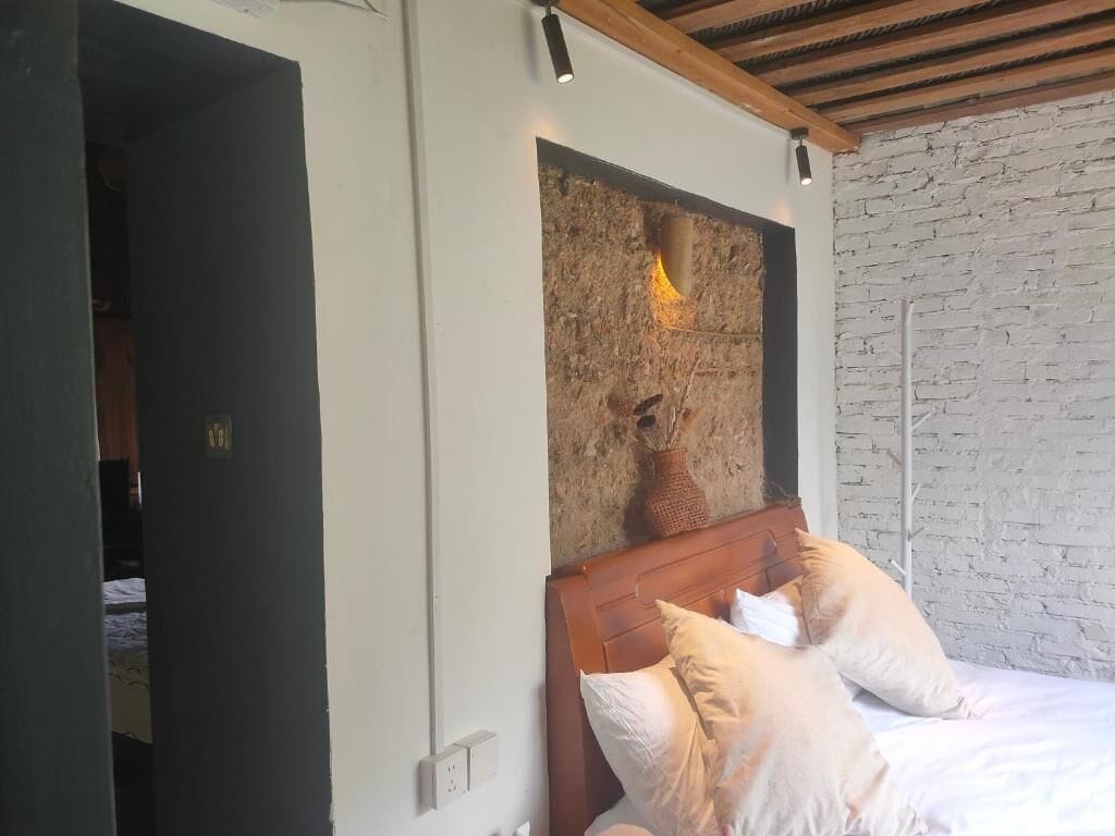 A bedroom with a bed, a wall-mounted light fixture, and a brick wall.