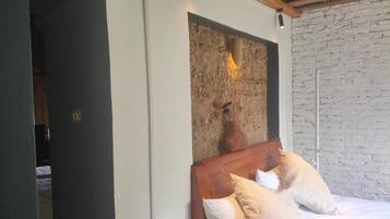 A bedroom with a bed, a wall-mounted light fixture, and a brick wall.