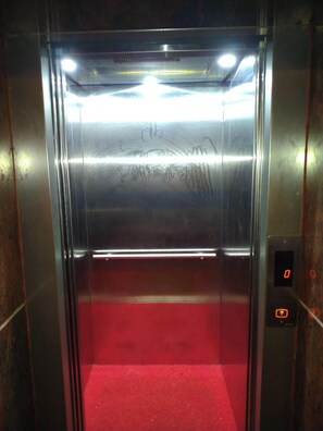 Un ascensor con paredes metálicas, una alfombra roja y una pantalla digital que muestra el número 0.